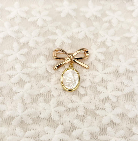 Delicate gold-tone bow baby brooch with dangling mother-of-pearl Guardian Angel charm – iridescent nacre angel medal set in gold rim, perfect Catholic baptism, christening, or blessing keepsake pin.