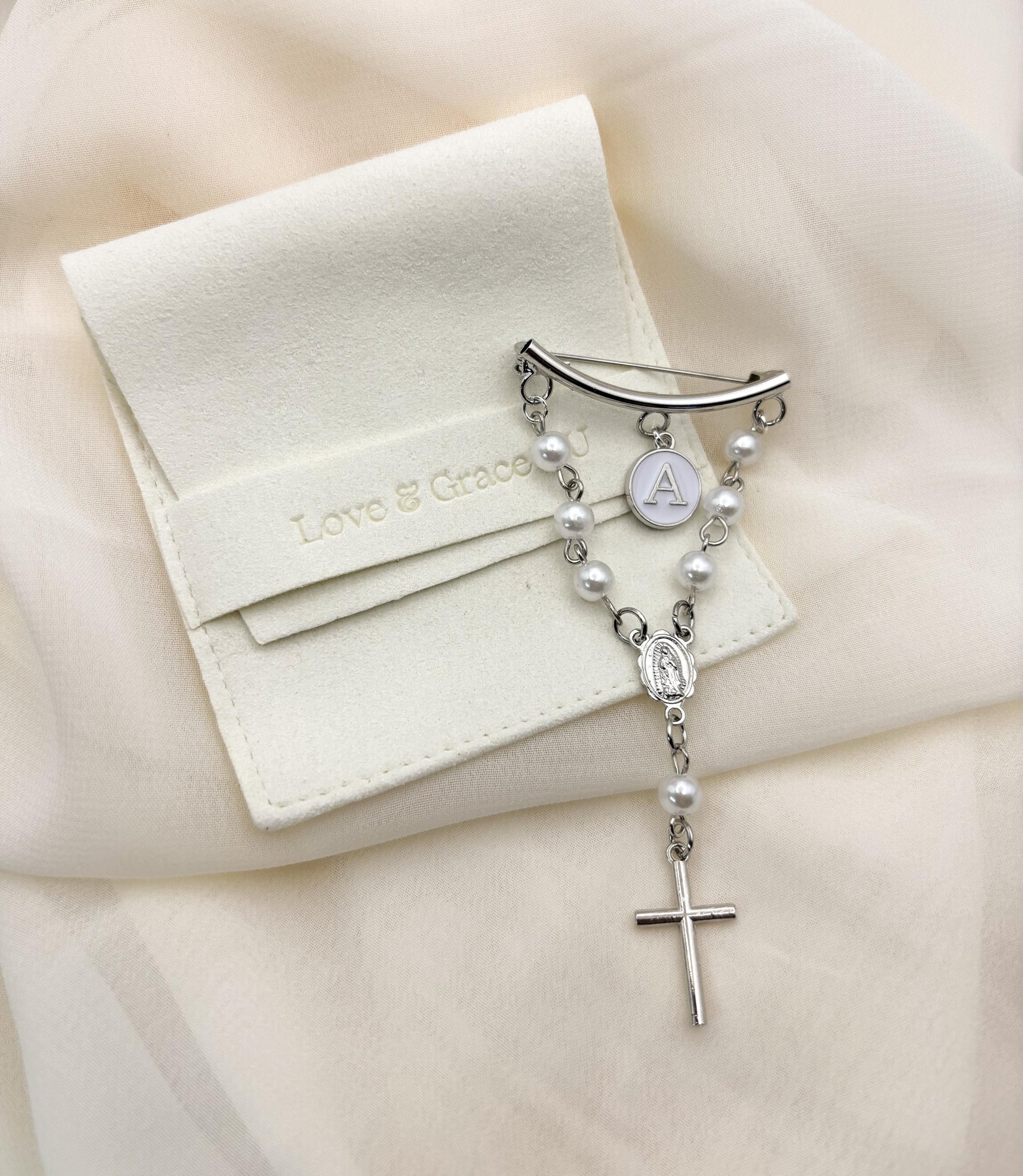 Personalized sterling silver rosary baptism pin for baby girls or boys: curved bar clasp with freshwater pearl chain, custom white letter charm, Our Lady of Guadalupe medal, and dainty silver cross. Packaged in elegant white satin pouch embossed &quot;Love & Grace.&quot; Hypoallergenic christening keepsake, newborn gift idea. Handcrafted Virgin Mary and Religious cross heirloom jewelry.