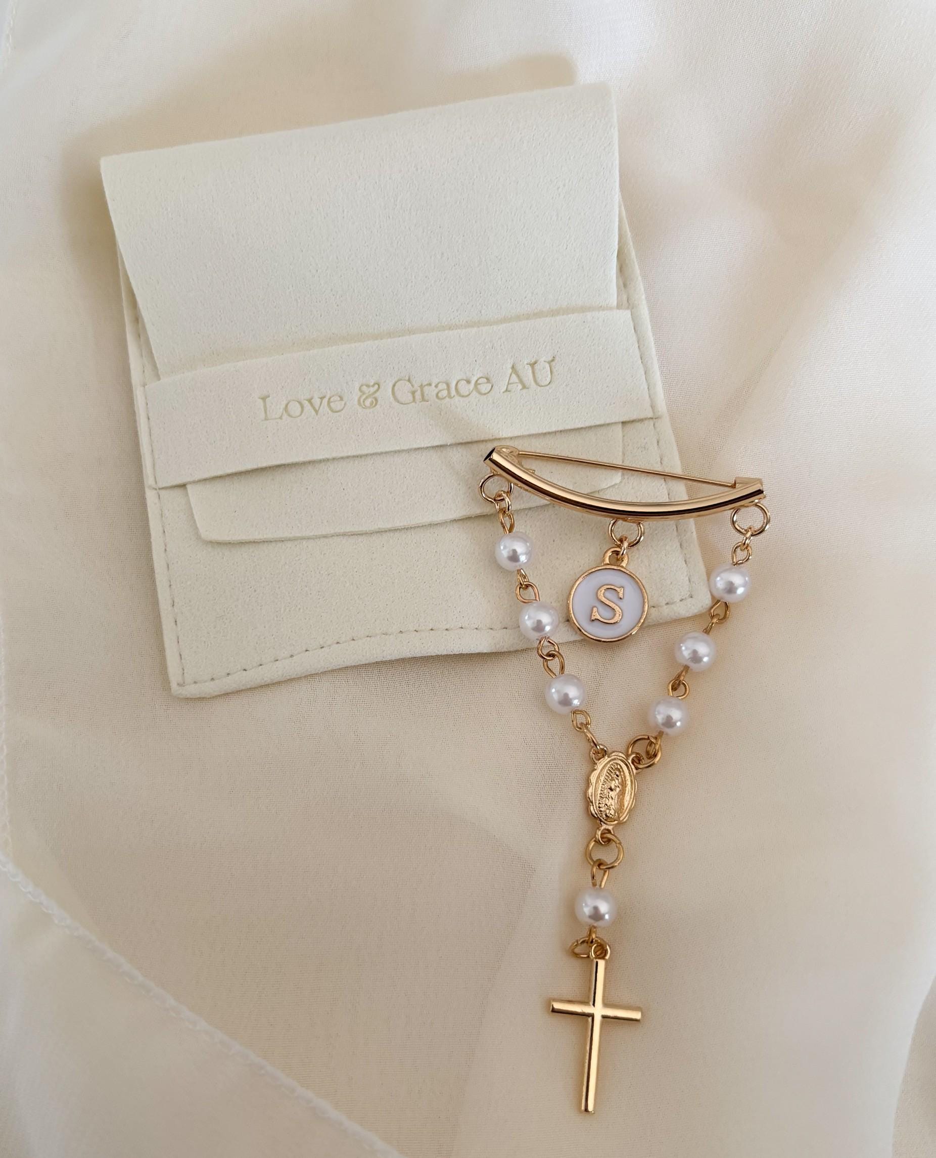 Delicate gold rosary chain adorned with pearls, featuring a curved gold bar brooch, personalized white enamel initial charm, Our Lady of Guadalupe medal, and petite gold cross. Elegantly presented in a soft white satin drawstring pouch monogrammed &quot;Love & Grace AU.&quot; Ideal baptismal or christening keepsake for baby girls. Handcrafted with love.